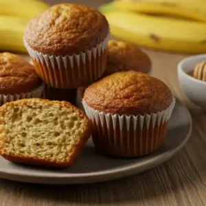 How to Make Classic Kodiak Banana Muffins Close-up of freshly Classic Kodiak banana muffins with a sliced muffin showing a soft texture, ripe bananas, and a honey drizzle.