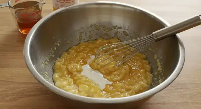 How to Make Classic Kodiak Banana Muffins A mixing bowl with mashed bananas, eggs, milk, and honey being whisked together for Kodiak banana muffins batter.