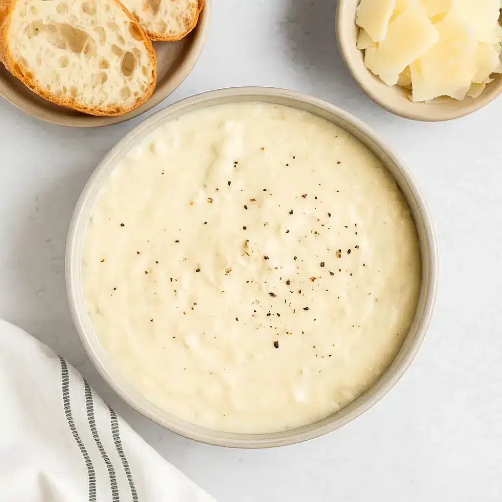alfredo sauce in ceramic bowl with crusty bread and parmesan
