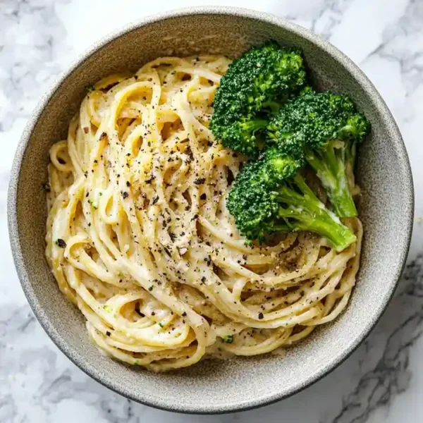 low calorie pasta alfredo with creamy sauce and broccoli served in a beige ceramic bowl