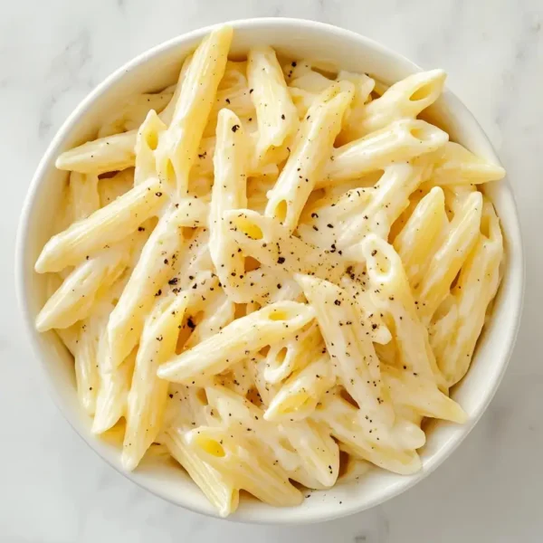 penne pasta in creamy alfredo sauce served in a white ceramic bowl.