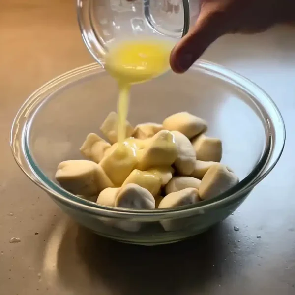 Quick and easy cinnamon roll bites being coated with melted butter in a glass bowl