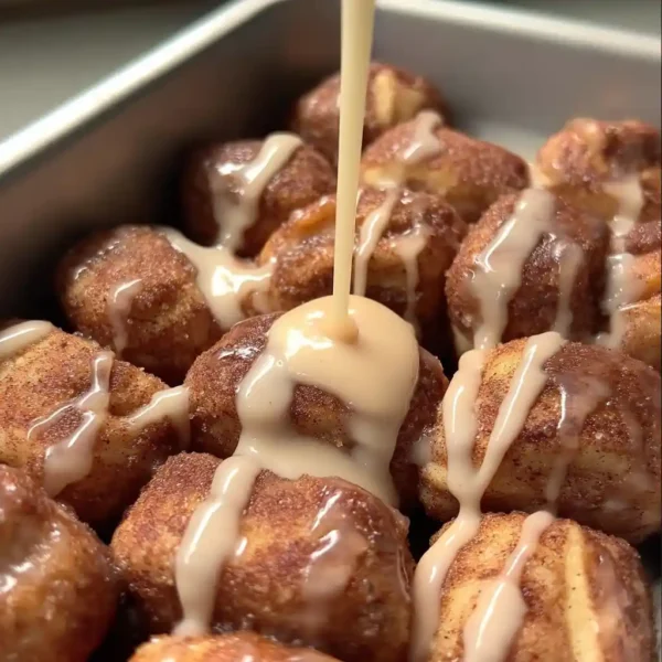 Quick and easy cinnamon roll bites being drizzled with vanilla glaze in loaf pan