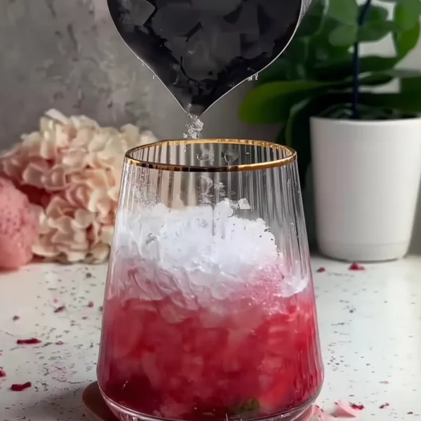 Raspberry Lime Mojito Mocktail in clear glass with crushed ice being poured in