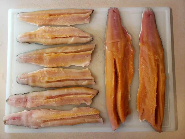 Smoked and raw lake trout fillets side by side on white cutting board