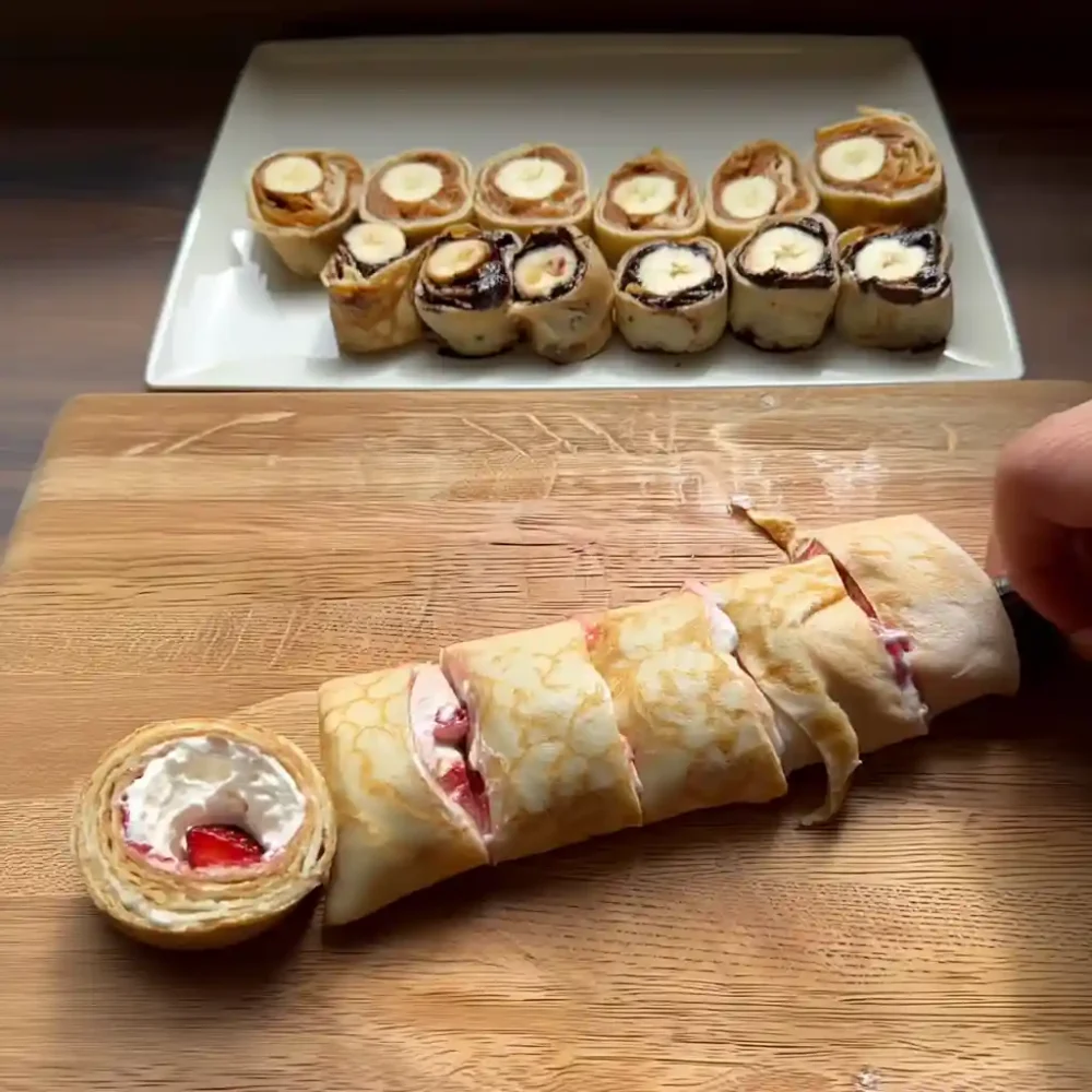 A rolled crepe with cream and fruit being sliced into sushi-style rounds