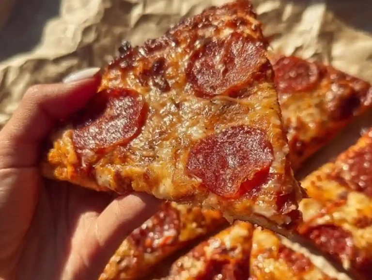 Chicken Crust Pizza slice with crispy pepperoni and melted cheese held in hand