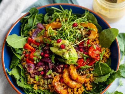A colorful bowl of roasted vegetables and quinoa drizzled with maple tahini dressing.