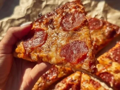 Chicken Crust Pizza slice with crispy pepperoni and melted cheese held in hand