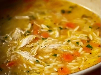 Bowl of lemon chicken orzo soup garnished with fresh herbs