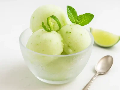 Lime sorbet in a frosted bowl with mint leaves and lime zest garnish on white background