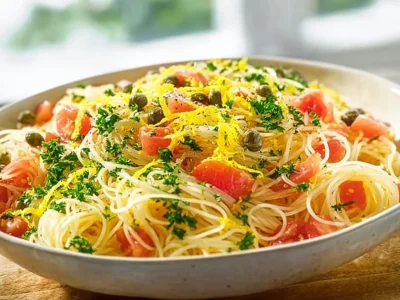 A colorful bowl of Pasta Salad with Capers and Tomatoes, garnished with fresh herbs.