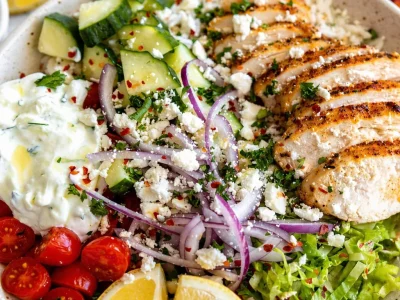 A colorful Greek Chicken Bowl with chicken, cucumber salad, tomatoes, and tzatziki.