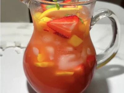 strawberry mango lemonade in a clear pitcher with ice, lemon slices, strawberry and mango chunks